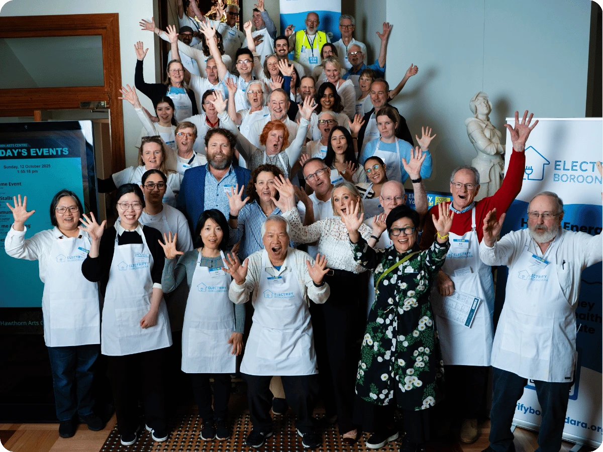 Electrify Boroondara volunteers in aprons cheering with their hands in the air at a community event